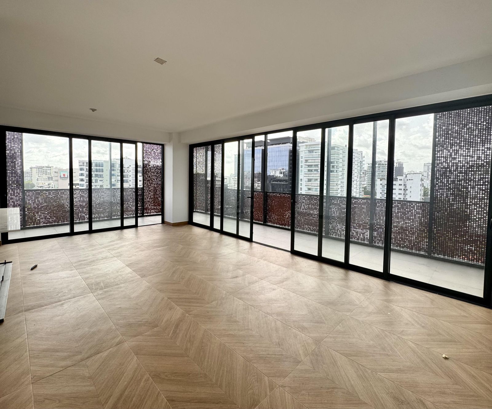 Sala principal con piso de espina de pescado y pared de cristal con vista a Piantini
